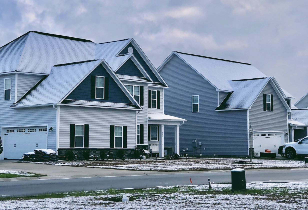 A snow-covered suburban home with blue siding